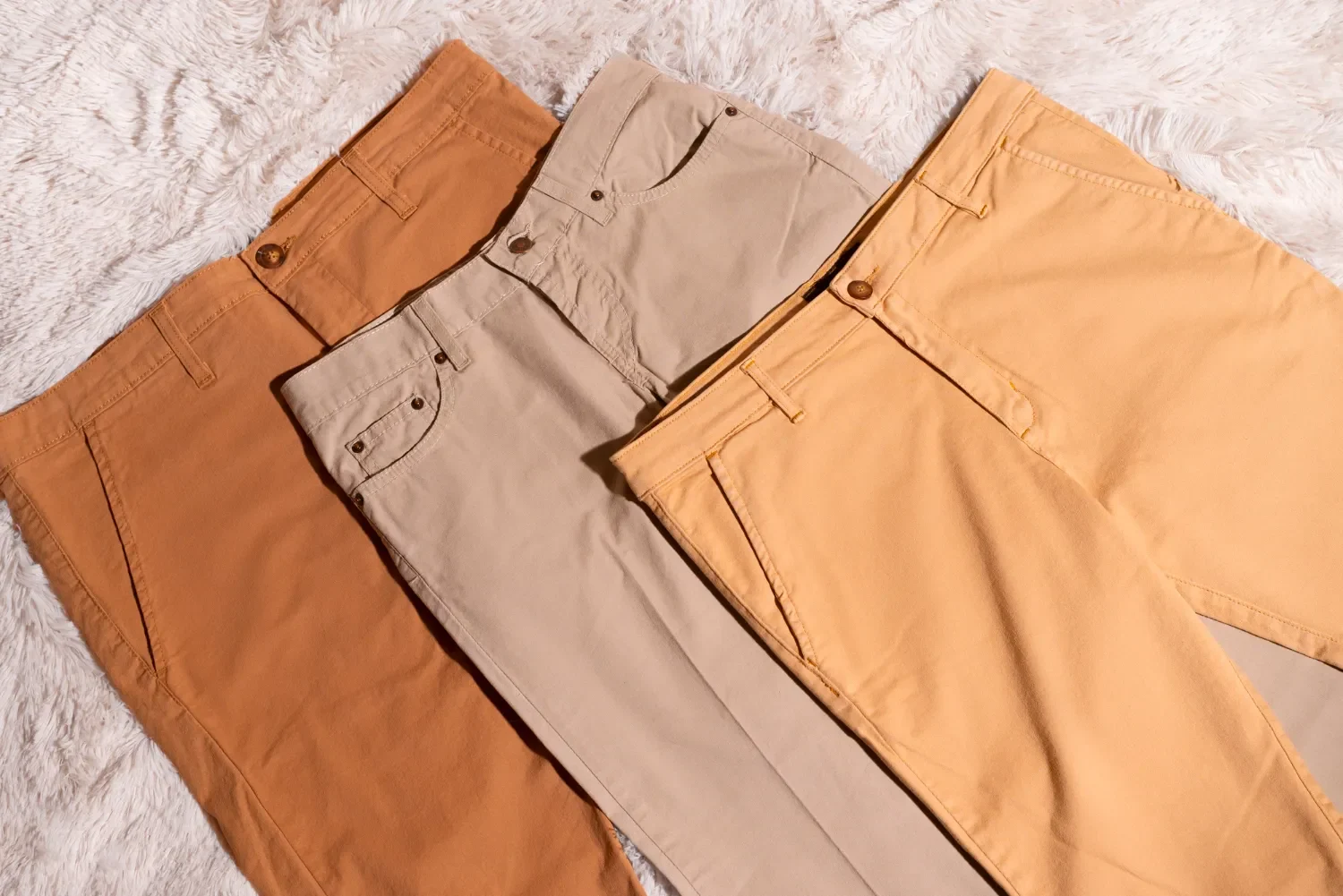Pantalones en tonos marrón, beige y amarillo dispuestos sobre una superficie suave. Ideal para moda masculina y femenina.